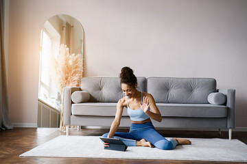 Home Sport. African american woman atching online tutorials on laptop and training on yoga mat in living room and enjoying fitness and healthy lifestyle	  