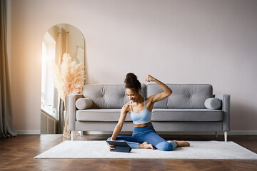 Home Sport. African american woman atching online tutorials on laptop and training on yoga mat in living room and enjoying fitness and healthy lifestyle	  