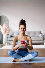 Home Sport. African american woman atching online tutorials on laptop and training on yoga mat in living room and enjoying fitness and healthy lifestyle