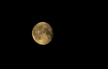 A yellow moon with clearly visible craters in a black night sky.
