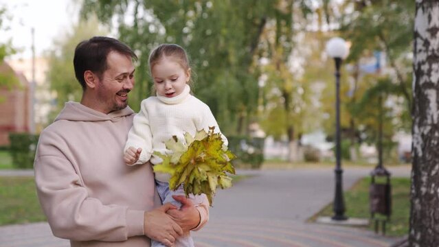 Active family, dad, little daughter, walk together in park in autumn. Father, child collect yellow maple leaves for walk. Happy childhood, fatherhood. Girl, dad, play on street. Family relationships