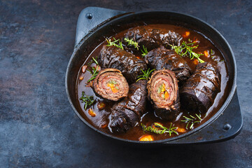 Traditionelle slow cooked deutsche Wagyu Rinderrouladen mit Gemüse und Speck in würziger Bratensoße als close-up in einem Design Topf