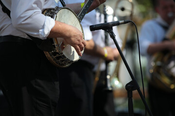 A musician with a banjo at the microphone on stage playing in an orchestra - obrazy, fototapety, plakaty