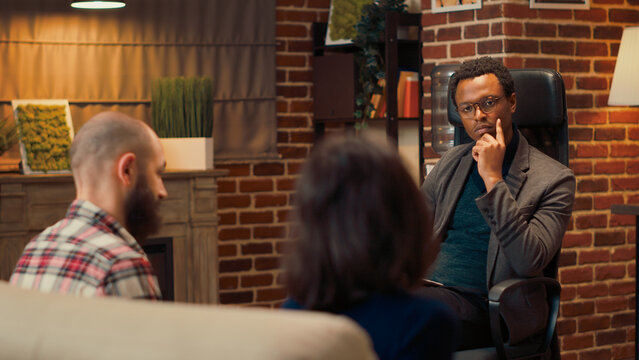 African american therapist taking notes at counseling session with married couple, talking about conflict and problems. Specialist consulting unhappy people in relationship at meeting.