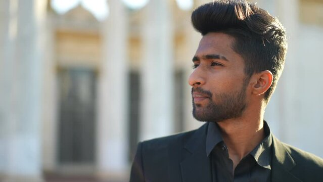 Close-up portrait of smiling Middle Eastern young man smoking talking standing on urban city street. Happy confident handsome guy in sunshine outdoors. Harmful habits and lifestyle concept