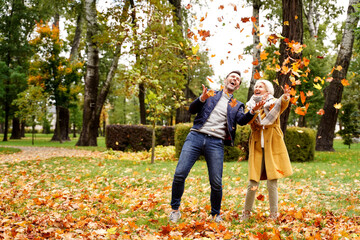 Happy married Couple having fun together outdoor in the golden autumn park, throwing leaves and laughing. Wife and husband in love. Real people emotions