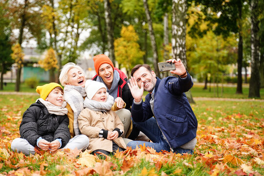 Family of five people spending time and having fun together, taking selfie on the mobile phone or talking online with someone at the autumn golden park.