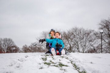 Two children slide down a snowy hill together in winter