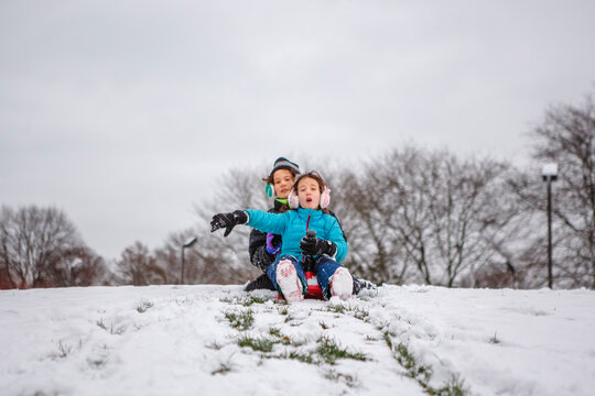 Two children slide down a snowy hill together in winter