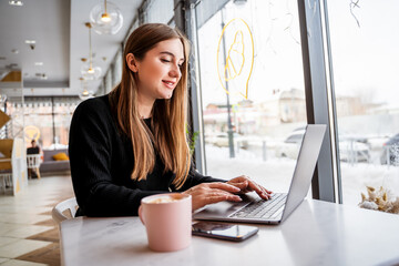 young girl sitting by the window at the laptop