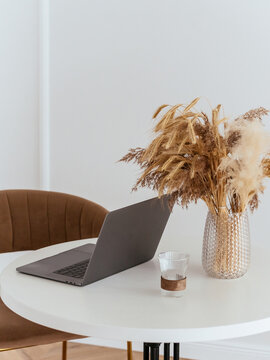 laptop on a white table with a vase and an autumn bouquet