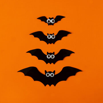 Four black bats with white eyes aligned verticaly on orange background. Spooky minimal creative concept for Halloween wallpaper or web banner or advertisement. Flat lay