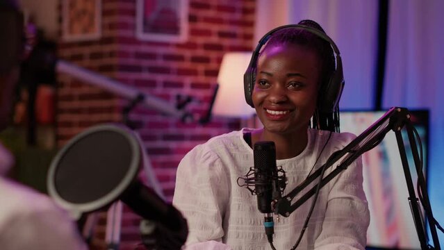 Closeup of african american podcaster in home recording studio in intervew with vlogger sitting at desk. Online radio host smiling confident at camera while broadcasting live with boom arm microphone.