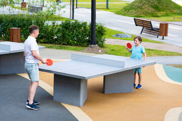 father and son play table tennis. dad teaches the child to play ping pong, father's day, healthy lifestyle. - obrazy, fototapety, plakaty
