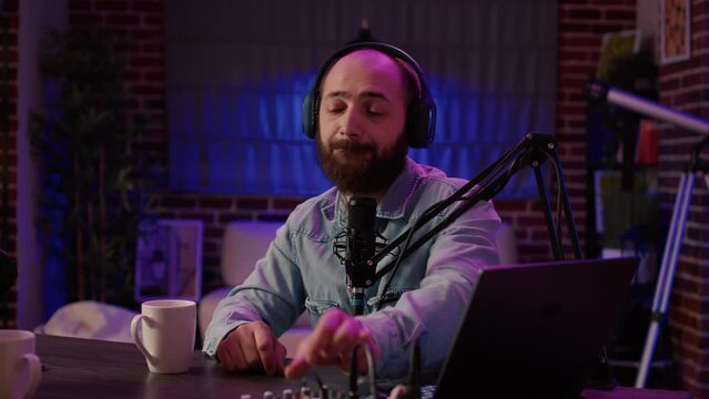 Online radio talkshow host pausing conversation with guest to answer live call from listener in home studio. Closeup of man recording podcast using professional audio equipment and microphone.