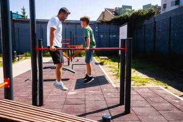 Father exercising with his son on  a dip station at outdoor gym