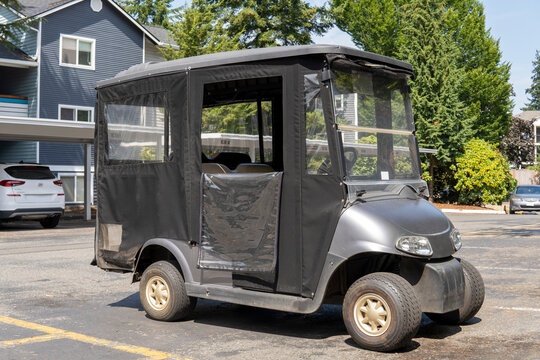 Black golf cart with a fabric awning stands in the yard. Everett, WA, USA - August 2022
