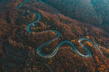 aerial photography of curved road on autumn, beautiful curved pass with vehicles and colorful autumn nature colors on trees with sunset light