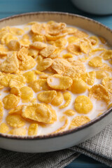 Bowl of tasty corn flakes on light blue wooden table, closeup