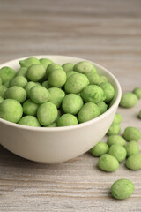 Bowl with tasty wasabi coated peanuts on white wooden table, closeup