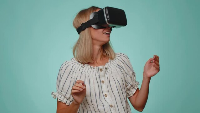 Amazed adult woman in shirt using headset helmet app to play simulation game. Watching virtual reality 3D 360 video. Young girl in VR goggles isolated on blue background. Addiction from new technology