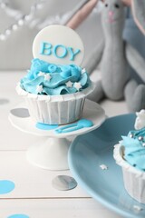 Delicious cupcake with light blue cream and Boy topper for baby shower on white wooden table