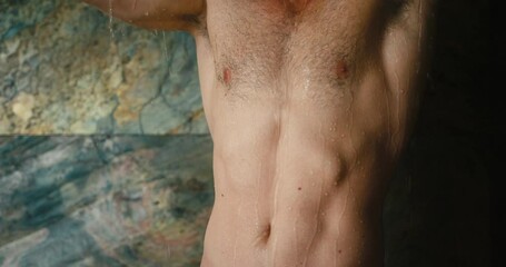 Muscular man takes shower enjoying caring of body health