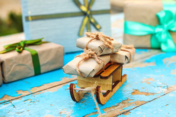 Close-up Xmas gift composition. Wrapped craft vintage gift boxes lying wooden toy sled on blue old wooden background. Present box in craft paper. Holiday concept.Christmas backdrop. Many eco present