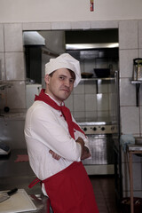 Young handsome chef posing in kitchen in restaurant. Portrait of positive male cook in uniform.