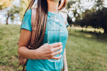 Unrecognizable girl wearing turquoise t shirt and holding a glass bottle with water in nature. Natural resource