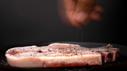 Close-up of chef cooking steak and putting spices on pan on black background.
