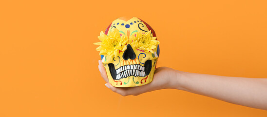 Fototapeta Hand holding painted skull and flowers on orange background. Celebration of Mexico's Day of the Dead (El Dia de Muertos) obraz