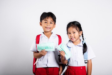 Two Asian student kid girl boy brother sister wearing student thai uniform holding protect mask ready to go to school in studio shot isolated on white background, new normal back to school