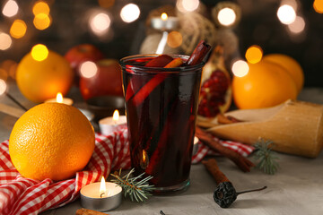 Glass of delicious mulled wine, oranges and candles on table