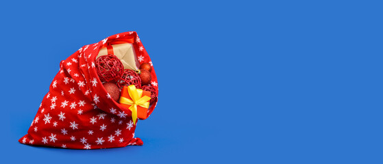 Santa Claus bag full of gifts and decorations on blue background with space for text
