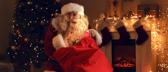 Santa Claus with bag showing silence gesture in room at Christmas night
