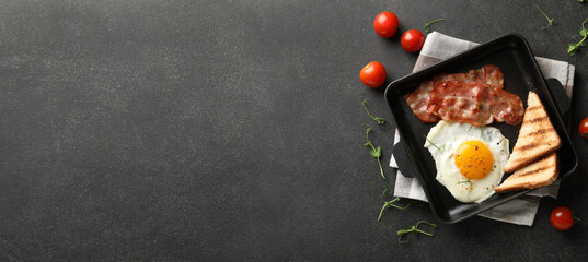 Frying pan with tasty sunny-side up egg, toasts and bacon on dark background with space for text