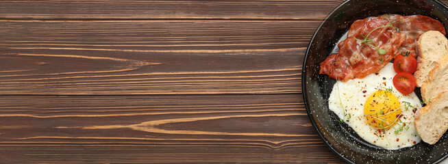 Frying pan with tasty sunny-side up egg, bread and bacon on wooden background with space for text