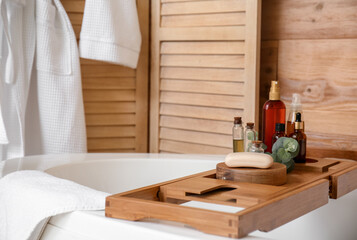 Wooden board with soap and bottles of cosmetics in bathroom