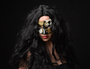 close up portrait of beautiful woman wearing fantasy masquerade mask with long black hair on dark studio background.