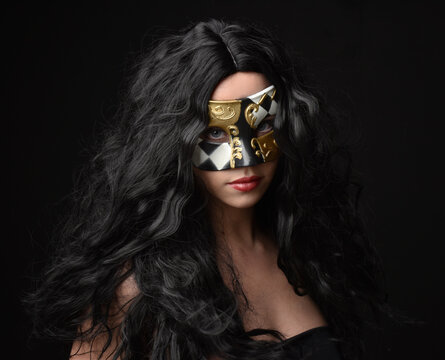 close up portrait of beautiful woman wearing fantasy masquerade mask with long black hair on dark studio background.