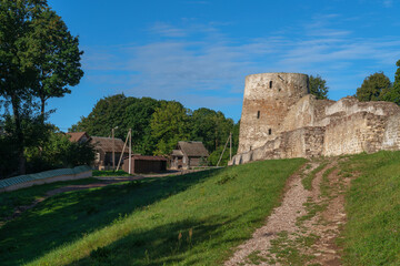 Fototapeta na wymiar View of the wall and tower of the Izborsk fortress against the background of a village on a sunny summer day, Izborsk, Pskov region, Russia