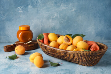 Wicker basket with tasty ripe apricots on color background