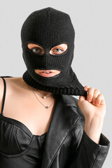 Portrait of young woman in balaclava against light background