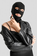 Young woman in balaclava holding red lipstick on light background