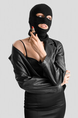 Young woman in balaclava holding red lipstick on light background