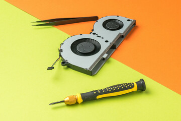 Tweezers, a screwdriver and a laptop fan on a green-orange background.