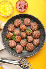 Frying pan with tasty meat balls, tongs, napkin and sauces on color background