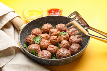 Frying pan with tasty meat balls and tongs on color background, closeup