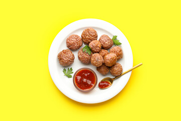 Plate with tasty meat balls, parsley, sauce and spoon on yellow background